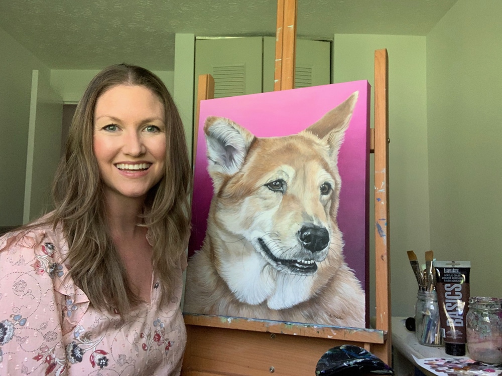 Fine arts painter Erica Eriksdotter sits by her easel with a custom painting of a black lab