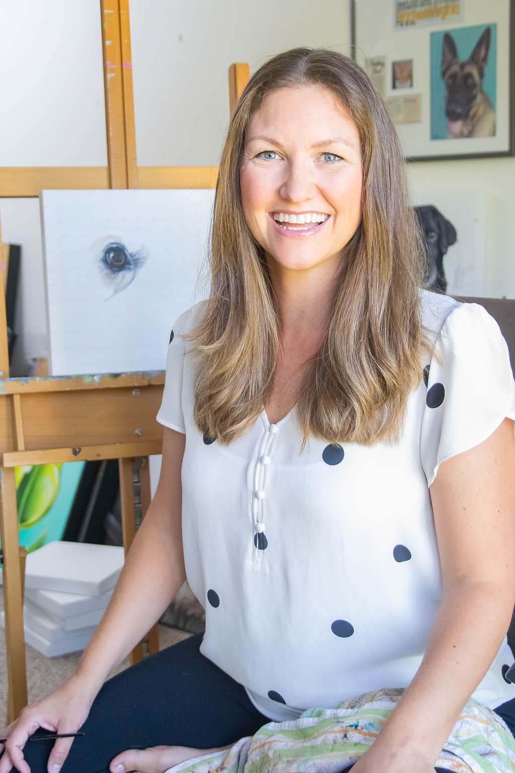 Erica Eriksdotter smiling in her studio, with custom pet portraits in progress in the background.