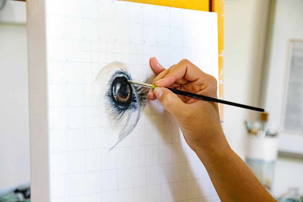 Erica Eriksdotter painting a custom pet portrait, focusing on a detailed animal eye on canvas.