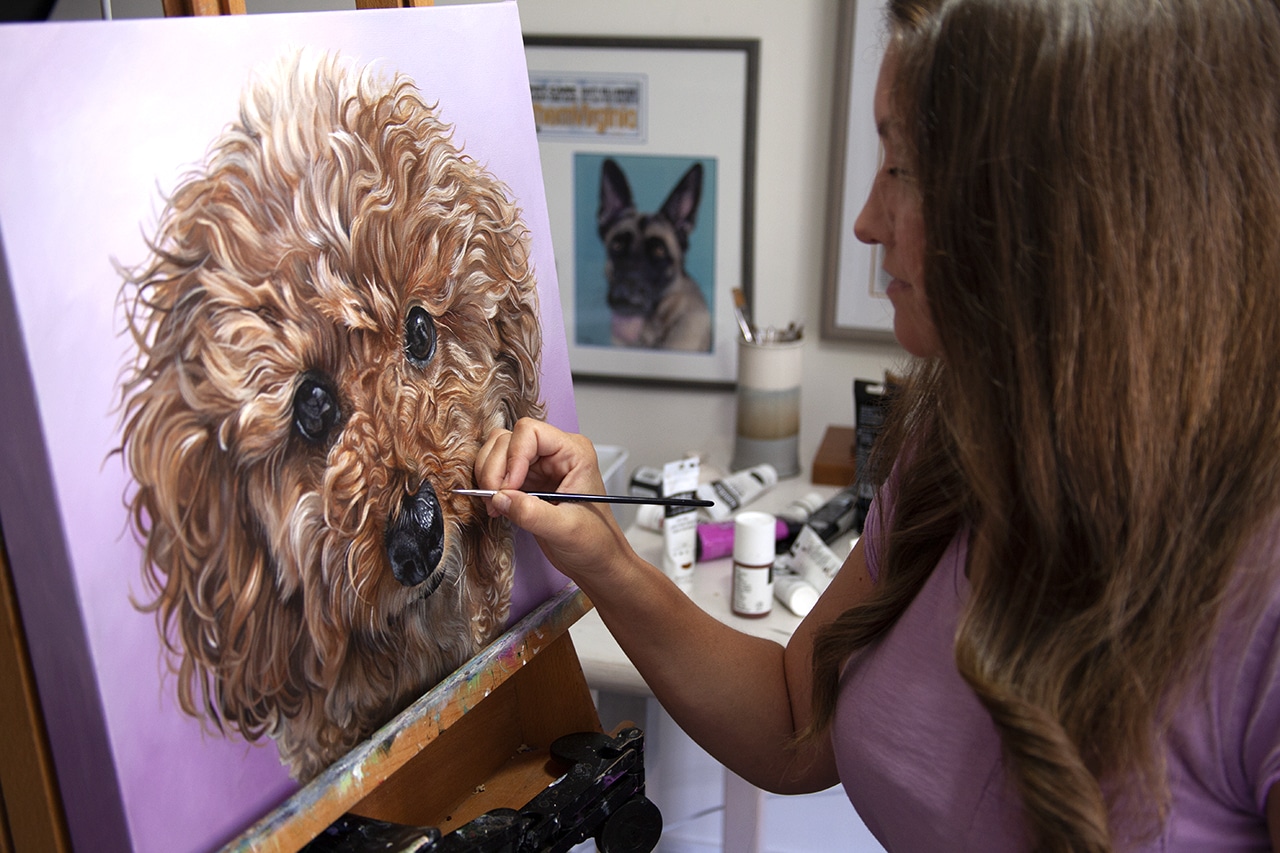 Artist, Erica Eriksdotter, painting a custom pet portrait painting of a copper colored curly dog on canvas.