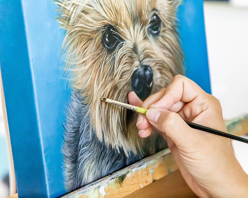 Close-up of artist, Erica Eriksdotter, painting a custom pet portrait painting of a brown dog on canvas.