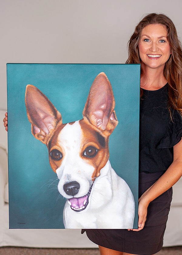 Artist, Erica Eriksdotter, holding a portrait of a white and red Jack Russel dog on canvas.
