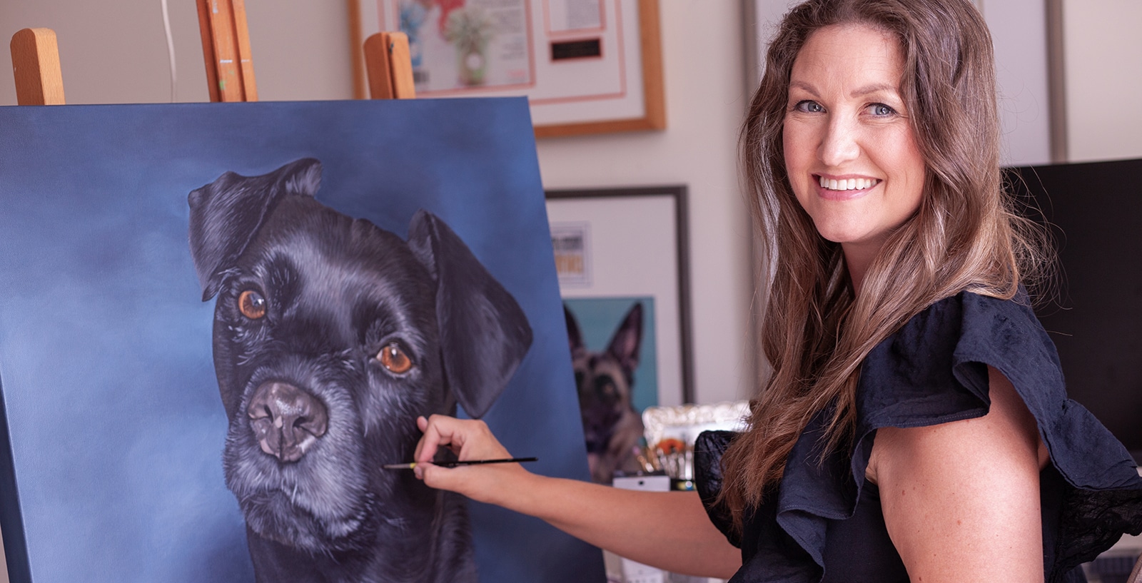 Artist, Erica Eriksdotter, painting a custom pet portrait of a black dog on canvas.