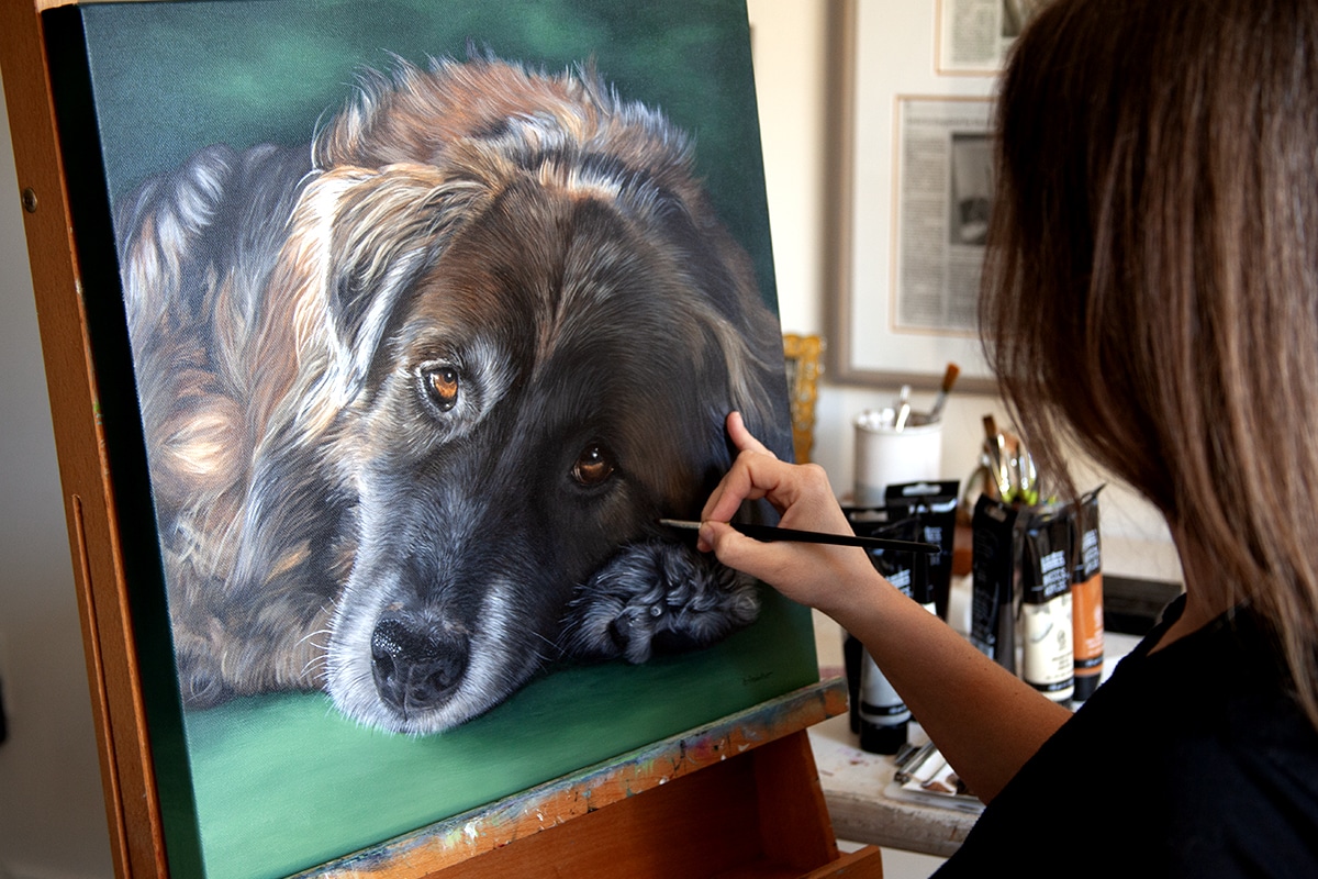 Artist, Erica Eriksdotter, painting a custom pet portrait painting of a brown dog on canvas.