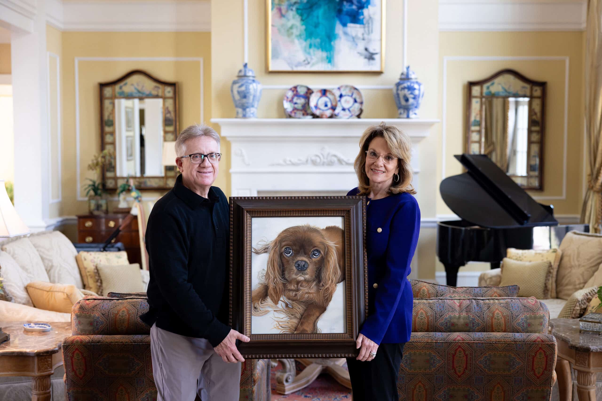 Tonya and Larry Smith holding a commissioned heirloom pet portrait of their late King Charles Spaniel, Rusty, painted by Erica Eriksdotter and featured in The New York Times.